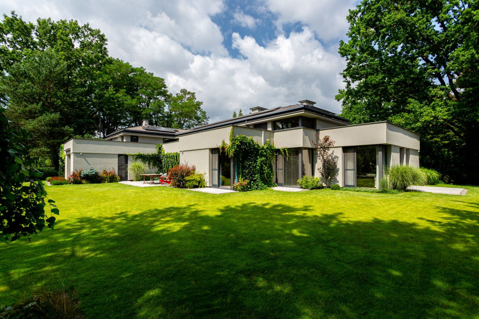 Nowoczesna rezydencja wybudowana przez generalnego wykonawcę New-House. Widoczna jasna elewacja, duże przeszklenia oraz w pełni zagospodarowany ogród z trawnikiem i nasadzeniami